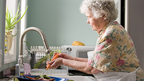 An elderly woman washing carrots at a kitchen sink.